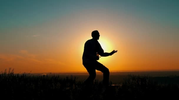 Человек весело играет на гитаре на восходе солнца — стоковое видео