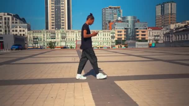 Glückliche Studentin nutzt Handy-Spaziergang in moderner Stadt — Stockvideo