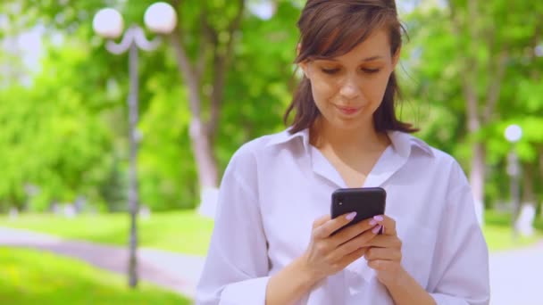 Красива дама з телефоном в руках в міському парку — стокове відео