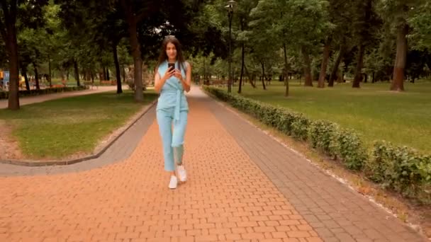 Νέος καυκάσιος γυναίκα χαρούμενος για τα καλά νέα περπατήματος στο δρόμο στο πάρκο της πόλης — Αρχείο Βίντεο