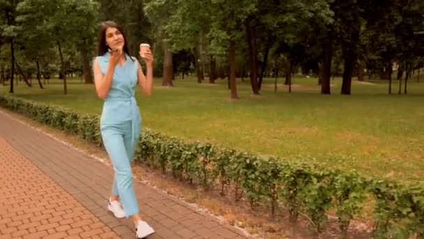 Молодая кавказская женщина отправляет звуковые сообщения с помощью мобильной прогулки по улице в городском парке — стоковое видео