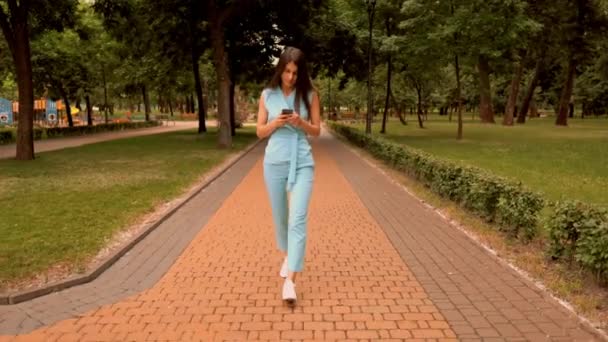 Joven mujer caucásica desplazamiento noticias alimentación caminando en la calle en el parque de la ciudad — Vídeos de Stock