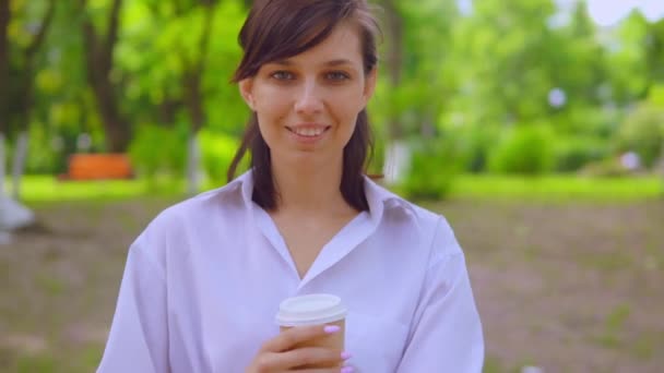Primer plano cara joven hembra en camisa blanca beber café en la calle — Vídeo de stock