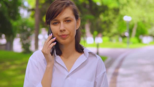 Portret millennials meisje heeft onderhandelingen gebruik maken van mobiele telefoon op de vlucht in park — Stockvideo