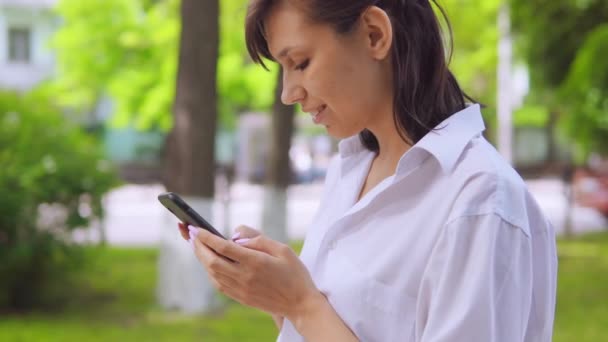 Vista lateral caucásico mujer chat en línea en el parque — Vídeo de stock