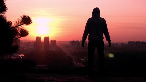 Силуэт мужчина на восходе солнца, поднимающиеся руки городской вид на город — стоковое видео