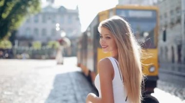 Sevimli genç kadınla bir bağsız kıl ile güzel bir beyaz elbiseli. Çekici genç hanım şehir merkezinde acele, kamera ve gülümsüyor için dönüyor. Ağır çekim