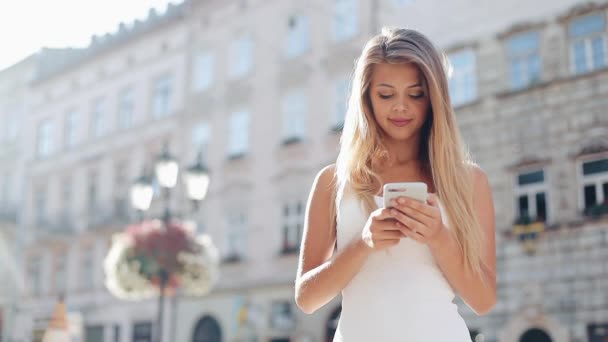 Giovane donna utilizzando smartphone e guardando nella fotocamera nella bella città europea. Rallentatore. Ragazza che naviga in Internet, cerca mappe e informazioni, comunica. Viaggio — Video Stock