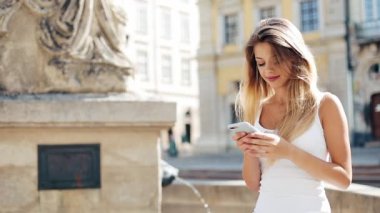 Avrupa şehirde Smartphone kullanan genç gülümseyen kadın. Meydanda Çeşme oturuyor. Internet tarama, haritalar ve bilgi arama, iletişim güzel kız. Seyahat