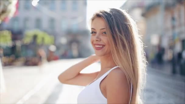 Charming young woman with a in a beautiful white dress with loose hair. Attractive young lady is rushing in the city-center, she turns to camera and smiles. Slow motion — Stock Video