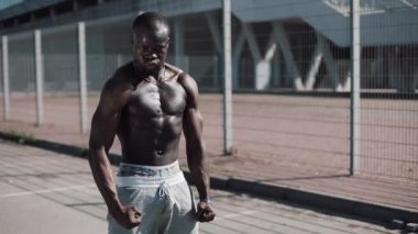Poz çıplak gövde ile atletik Afrikalı-Amerikalı adam açık havada kasları gösterir. Siyah adam stadium yanında poz kasları gösterir. Vücut geliştirme, poz, sağlık, fitness, güzellik.