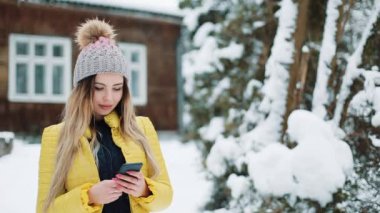 Mutlu genç kız smartphone, gülümseyen ve cep telefonunda manifatura app kullanarak. Kır evi bir kış ceket giyen kadın. İletişim, seyahat, bir yaşam tarzı kavramı. Kırmızı Epic vurdu