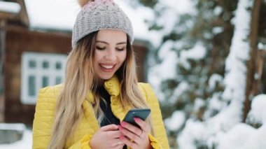 Mutlu genç kız smartphone, gülümseyen ve cep telefonunda manifatura app kullanarak. Kır evi bir kış ceket giyen kadın. İletişim, seyahat, bir yaşam tarzı kavramı. Kırmızı Epic vurdu