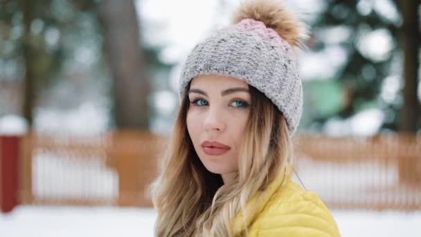 Чарівна жінка з блакитними очима стенди в зимовий капелюх в лісі покриті снігом. Портрет посміхається дівчина, насолоджуючись зимовий час. Постріл на червоний епос — стокове відео