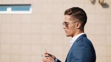 Genç businesman güneş gözlüğü ve para sayma ve sokakta yürürken bir takım elbise. Kazanç, başarılı iş seyahatleri, modern yaşam