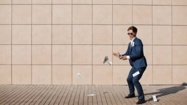 Genç işadamı dağılım dolar ve sokakta dans mutlu. Bu office center yanında, ağır çekim yer almaktadır. Başarılı iş