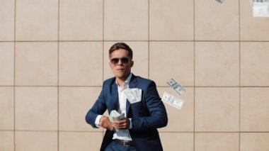 Mutlu genç işadamı dağılım dolar ve komik sokakta dans. Office center yanında, ağır çekim yürüyebiliyor. Para yağmur, başarılı iş