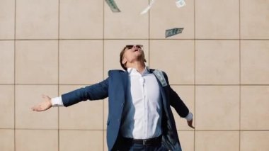 Mutlu genç işadamı dağılım dolar ve komik sokakta dans. Office center yanında, ağır çekim yürüyebiliyor. Para yağmur, başarılı iş