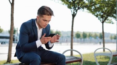 Kötü haber de sokakta bankta okuma smartphone ile mutsuz işadamı. Üzgün satış acentası Menkul Kıymetler Borsası kötü haber smartphone telefon sorun ekonomi kriz