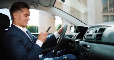 Genç yakışıklı işadamı cep telefonu arabaya kullaranarak. Mutlu genç adam başarılı olur ve bir ileti yazar. İletişim, başarılı iş, mobil teknoloji kavramı