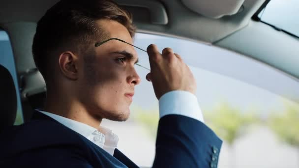 Joven hombre de negocios con gafas de sol mientras está sentado en un coche. Está sentado detrás del volante. Concepto de éxito, crecimiento profesional, negocio exitoso — Vídeos de Stock