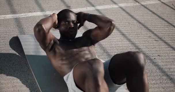 El atlético afroamericano está haciendo crujidos en una alfombra gris en la calle. Concepto de salud y estado físico. 4k, disparo en tiempo real — Vídeo de stock