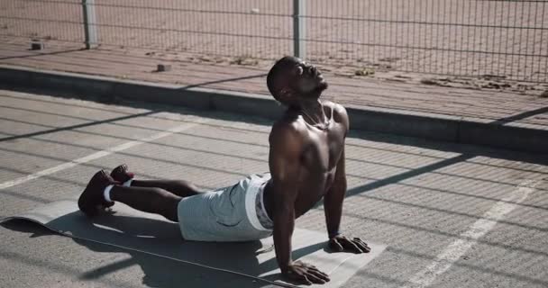 Homme afro-américain athlétique effectuant une planche à l'entraînement de rue.Entraînement de jeune homme dans l'entraînement de gars de sport près du stade de sport. Entraînement cross fit. Musclé noir homme poussant en plein air — Video
