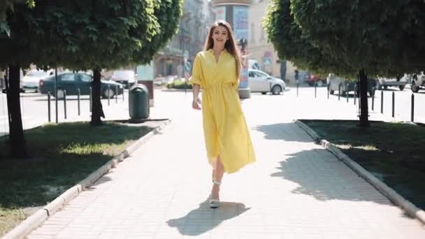 Hermosa chica en vestido amarillo caminando por la calle de la ciudad. Fondo borroso día soleado verano sol mujer sonriendo bonita mirada encantadora mirando cámara sonrisas alegre cara emocional ocio — Vídeo de stock