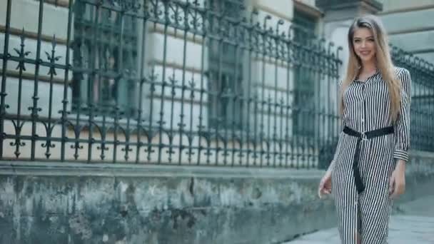 Feliz hermosa mujer de negocios en el hermoso vestido caminando a lo largo de la vieja calle. En cámara lenta. aspecto elegante. El concepto de un aspecto elegante y un negocio exitoso — Vídeos de Stock