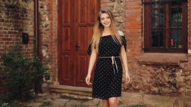 Menina bonita em vestido preto andando ao longo da rua cidade velha. Dia ensolarado verão sol mulher sorrindo muito linda olhar olhar câmera sorrisos feliz emocional rosto lazer. Movimento lento — Vídeo de Stock