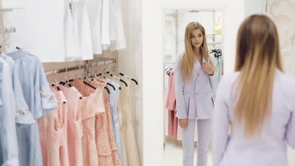 Attractive young businesswoman trying on dress and looking in mirror to see how she looks in it. Brautiful girl trying on her suit in shop and admiring her reflection in the mirror. Slow motion — Stock Video