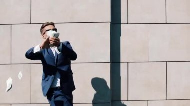 Mutlu genç işadamı dağılım dolar ve komik sokakta dans. Para yağmur, düşen dolar. Bu office center yanında, ağır çekim yer almaktadır. Başarılı bir iş. Kırmızı Epic vurdu