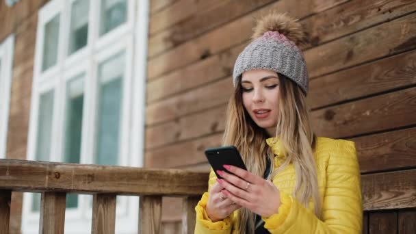 Gülümseyen kadın türlerinde arka bahçesinde üzerinde ayakta dışında telefon. Kır evi bir kış ceket giyen kadın. İletişim, seyahat, bir yaşam tarzı kavramı. Kırmızı Epic vurdu — Stok video