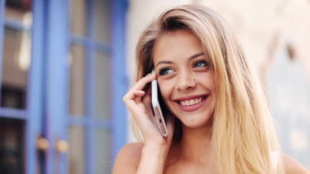 Gelukkig jonge vrouw in een mooie witte jurk praten over de status van de mobiele telefoon op straat. Close-up, langzame motie. — Stockvideo