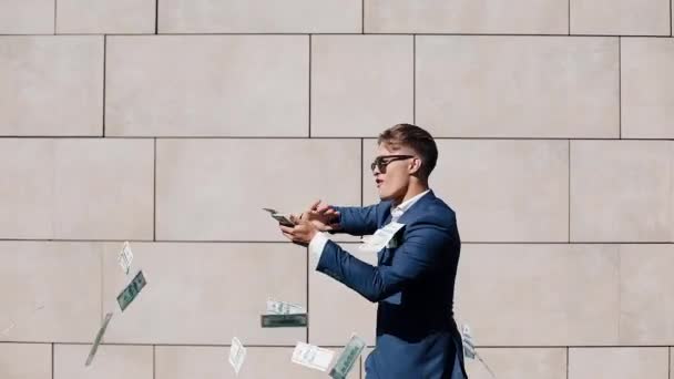 Young happy businessman scatter the dollars and funny dancing in the street. Money rain, falling dollars. It is located near the office center, slow motion. Successful business. Shot on Red Epic — Stock Video