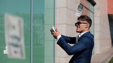 Mutlu genç işadamı dağılım dolar ve komik sokakta dans. Para yağmur, düşen dolar. Bu office center yanında, ağır çekim yer almaktadır. Başarılı bir iş. Kırmızı Epic vurdu