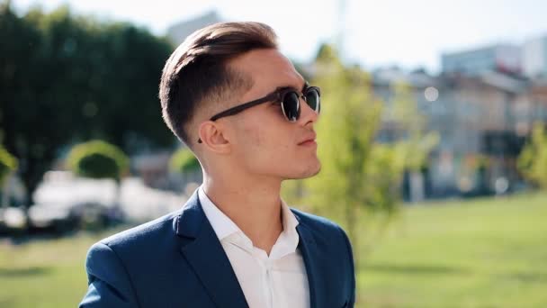 Joven empresario exitoso en gafas de sol de pie al aire libre. Se quita las gafas y mira a la cámara. Elegante atuendo elegante. Ser un jefe, estilo de vida exitoso — Vídeos de Stock