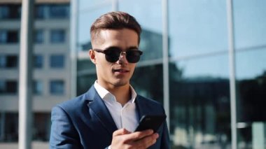 Genç businesman smartphone kullanarak ve sokakta yürürken güneş gözlüğü. Başarılı bir hayat. İş tarzı, Gezgin, iletişim, modern yaşam tarzı. Aktif yaşam tarzı