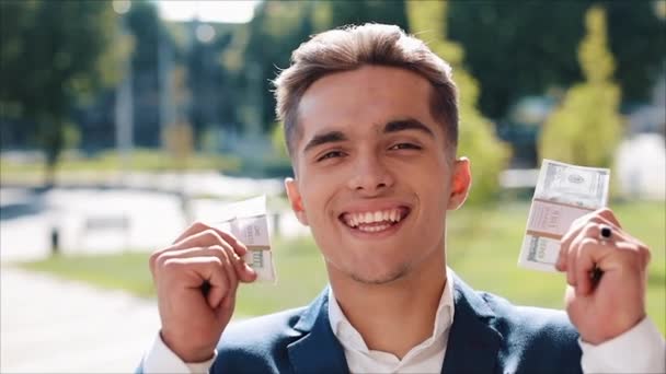 Χαρούμενος νεαρός επιχειρηματίας κρατώντας ένα μεγάλο ποσό των χρημάτων στα χέρια του. Στέκεται στο δρόμο κοντά στο κέντρο του office ή την Τράπεζα. Επαγγελματικό στιλ, τα κέρδη, κατάθεση, επιτυχία καριέρα — Αρχείο Βίντεο