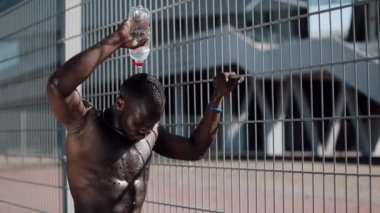Afro-Amerikan erkek atlet içme suyu şişe su yüzüne çalıştırdıktan sonra aşağı soğutma Caddesi üzerinde egzersiz. Yoğun egzersiz siyah adam. Ağır çekim