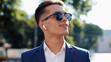 Çekici genç işadamı dışında yürüyüş kablosuz kulaklık kullanarak telefonda konuşuyor. Mutlu bir adam görüşmeler. İletişim, finans, iş adamları, stajyerler, Ceo. Yakın çekim. Kırmızı Epic vurdu