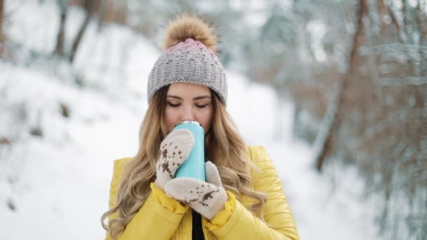 Mujer bonita en sombrero de invierno disfruta de la nieve y bebidas calientes de pie fuera en la nieve en el bosque. Chica disfrutando del invierno al aire libre. Vacaciones de Navidad — Vídeos de Stock