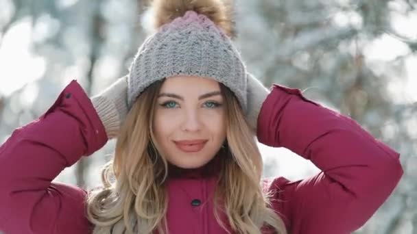 Красива жінка в зимовому капелюсі посміхається, стоячи на вулиці на снігу в лісі. Портрет красивої дівчини, яка дивиться в камеру. Зимовий час Відпочинок, зимові канікули, Різдво, відпустка — стокове відео
