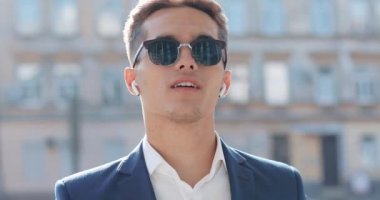 Çekici genç işadamı dışında yürüyüş kablosuz kulaklık kullanarak telefonda konuşuyor. Mutlu bir adam görüşmeler. İletişim, finans, iş adamları, stajyerler, Ceo. Yakın çekim. Kırmızı Epic vurdu