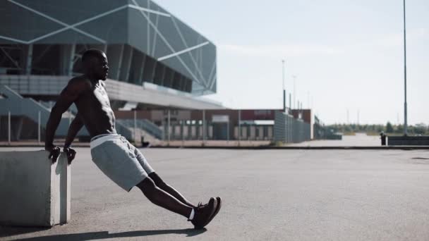 Entrenamiento callejero. Atlético hombre afroamericano haciendo flexiones y ejercicios de spinning al aire libre. Un hombre negro está practicando deportes cerca del estadio. Entrenamiento, fitness, correr, motivación — Vídeos de Stock