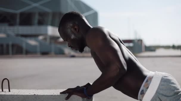 Allenamento stradale. Uomo afroamericano atletico che fa flessioni ed esercizio di spin all'aperto. Un uomo nero sta facendo sport vicino allo stadio. Allenamento, fitness, corsa, motivazione — Video Stock