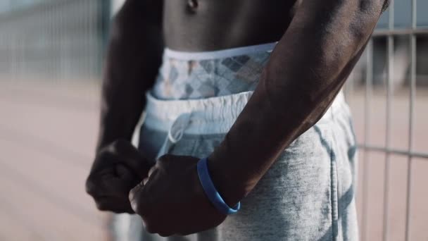 Man showing a perfect ABS. Muscular black man bodybuilder. Man posing standing outside near sport stadium, shows his muscles. Shot on Red Epic — Stock Video