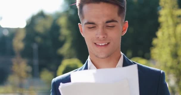 Joven hombre de negocios feliz en un traje elegante examina cuidadosamente los papeles al aire libre. Estilo de vida exitoso, contrato, responsabilidad. Negocios, personas, concepción del papeleo — Vídeos de Stock