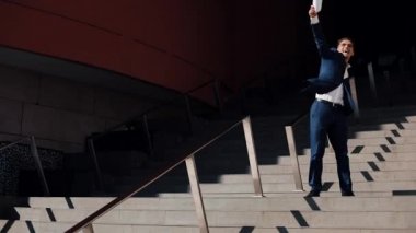 Genç başarılı işadamı ofis binası ile imzalanmış bir sözleşme bırakır. O mutlu ve komik sokakta dans. Ağır çekim. İş, evrak, tatil, sözleşme, yaşam biçimi