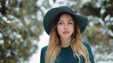 Bayan yeşil palto ve şapka etrafında kış Ormanda yürür. Bir kış parkta şık genç güzel kadın portresi kadar karlı arka plan üzerinde kapatın. Kış park kamera için arıyorum. Açık havada